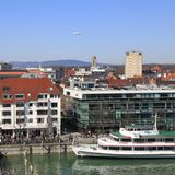 Die Uferpromenade von Friedrichshafen am Bodensee. Am Himmel fliegt ein Zeppelin.