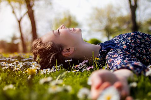 Junge Frau liegt in Blumenwiese und lacht