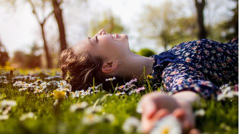 Junge Frau liegt in Blumenwiese und lacht