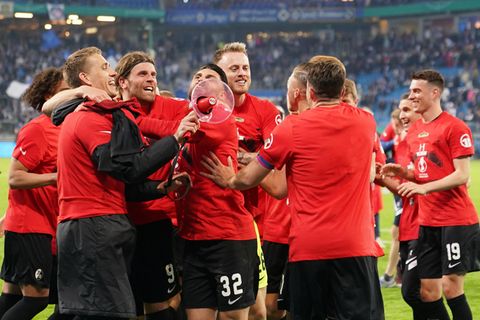 Eine Grußße Fußballer in roten T-Shirts jubeln gemeinsam, während einer von ihnen ein rotes Megafon in der Hand hält