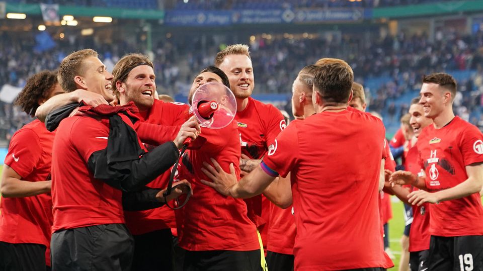 Eine Grußße Fußballer in roten T-Shirts jubeln gemeinsam, während einer von ihnen ein rotes Megafon in der Hand hält