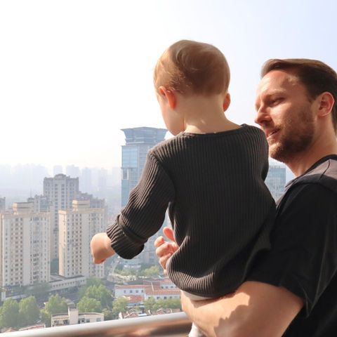 Junger Mann mit Kleinkind auf dem Arm steht auf einem Balkon