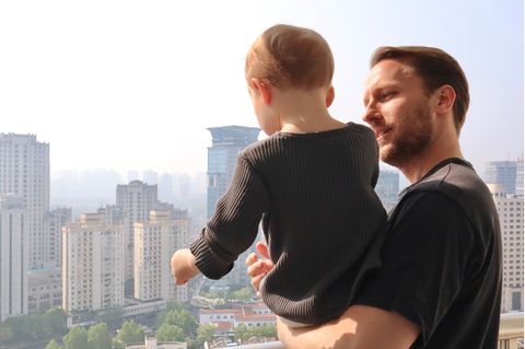 Junger Mann mit Kleinkind auf dem Arm steht auf einem Balkon
