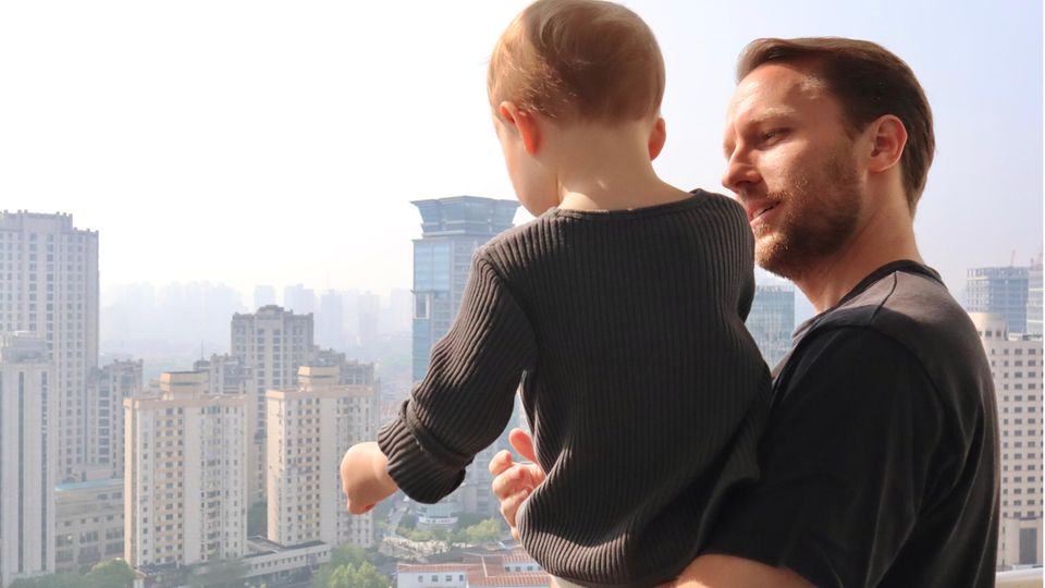 Junger Mann mit Kleinkind auf dem Arm steht auf einem Balkon