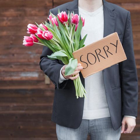 Ein Mann hat einen Strauß Tulpen udn ein Schild mit dem Wort "Sorry" in der Hand