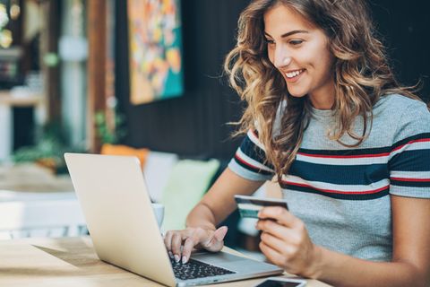 Eine Frau sitzt mit Kreditkarte in der Hand am Laptop