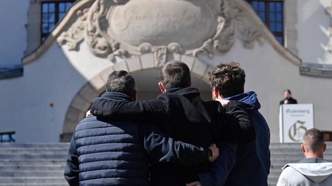 Drei Jugendliche umarmen sich im stillen Gedenken vor dem Schulgebäude in Erfurt am 19. Jahrestag des Schulmassakers