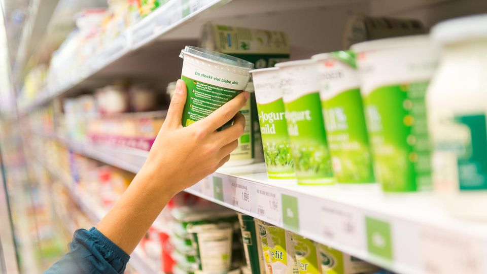 Frau holt Joghurtbecher aus dem Supermarkt-Regal