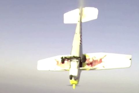 Ein weiß, gelb und rot lackiertes Sportflugzeug mit Propeller stürzt auf den Boden zu
