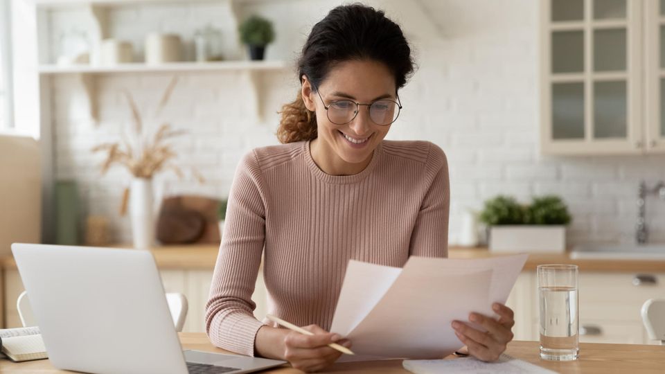 Eine Frau sitzt mit einer Rechnung vor ihrem Laptop