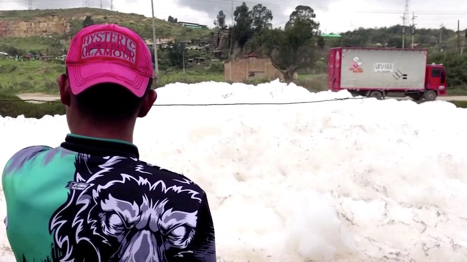 Ein junger Mann ist von hinten zu sehen. Mit rotem, umgedrehtem Basecap auf dem Kopf schaut er auf einen Schaumberg auf Wasser Ein junger Mann ist von hinten zu sehen. Mit rotem, umgedrehtem Basecap auf dem Kopf schaut er auf einen Schaumberg auf Wasser