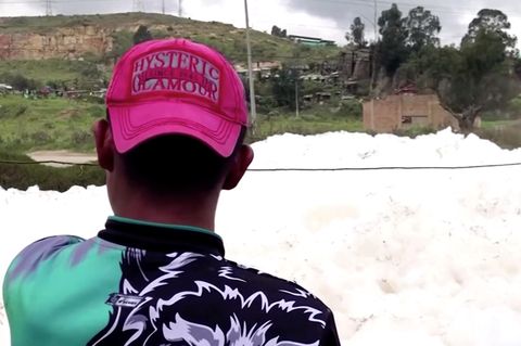 Ein junger Mann ist von hinten zu sehen. Mit rotem, umgedrehtem Basecap auf dem Kopf schaut er auf einen Schaumberg auf Wasser