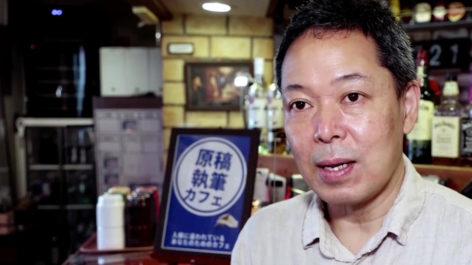 Ein asiatisch aussehender Mann spricht, während er vor einem hölzernen Tresen steht