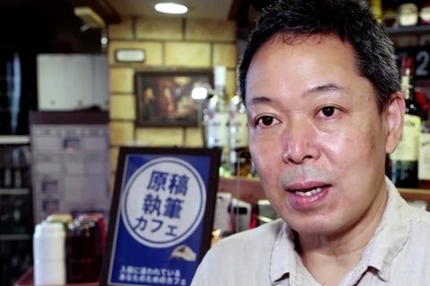 Ein asiatisch aussehender Mann spricht, während er vor einem hölzernen Tresen steht