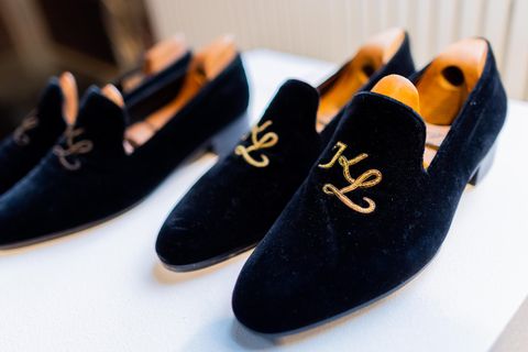 Blaue Samt-Slipper mit goldenem "KL"-Monogramm stehen auf einem weißen Podest