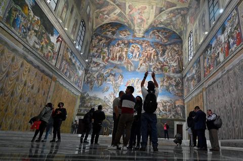 Menschen stehen verstreut in einer sonst leeren Kirche mit bemalten Wänden und Decken