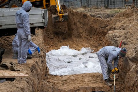 Ukraine, Butscha: Männer in Schutzkleidung exhumieren Leichen von Zivilisten