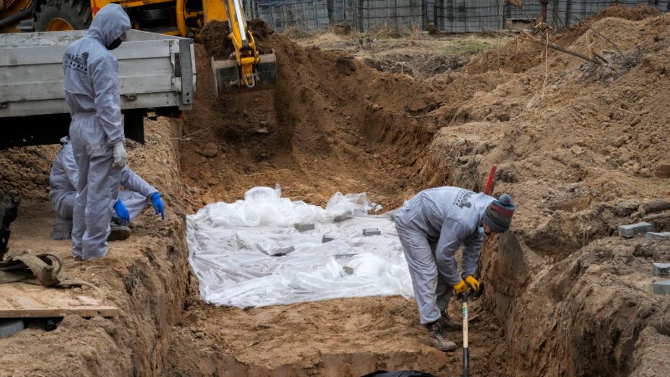 Ukraine, Butscha: Männer in Schutzkleidung exhumieren Leichen von Zivilisten