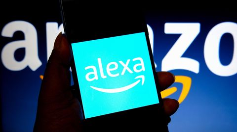Auf einem Smartphone-Bildschirm steht "Alexa", dahinter das Logo von Amazon