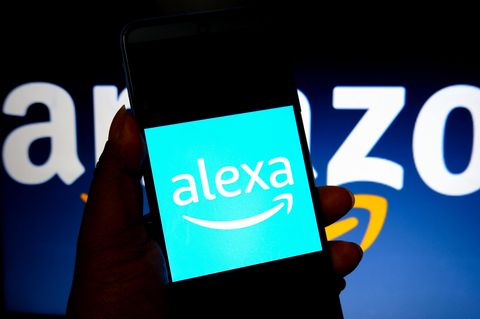 Auf einem Smartphone-Bildschirm steht "Alexa", dahinter das Logo von Amazon