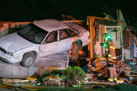 Ein Feuerwehrmann neben einem völlig zerstörten Haus, in dem ein Auto hängt