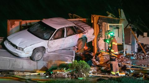 Ein Feuerwehrmann neben einem völlig zerstörten Haus, in dem ein Auto hängt