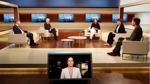 In einem in Blau und Creme gehaltenem TV-Studio sitzen drei Frauen und zwei Männer auf hellen Sesseln mit Abstand
