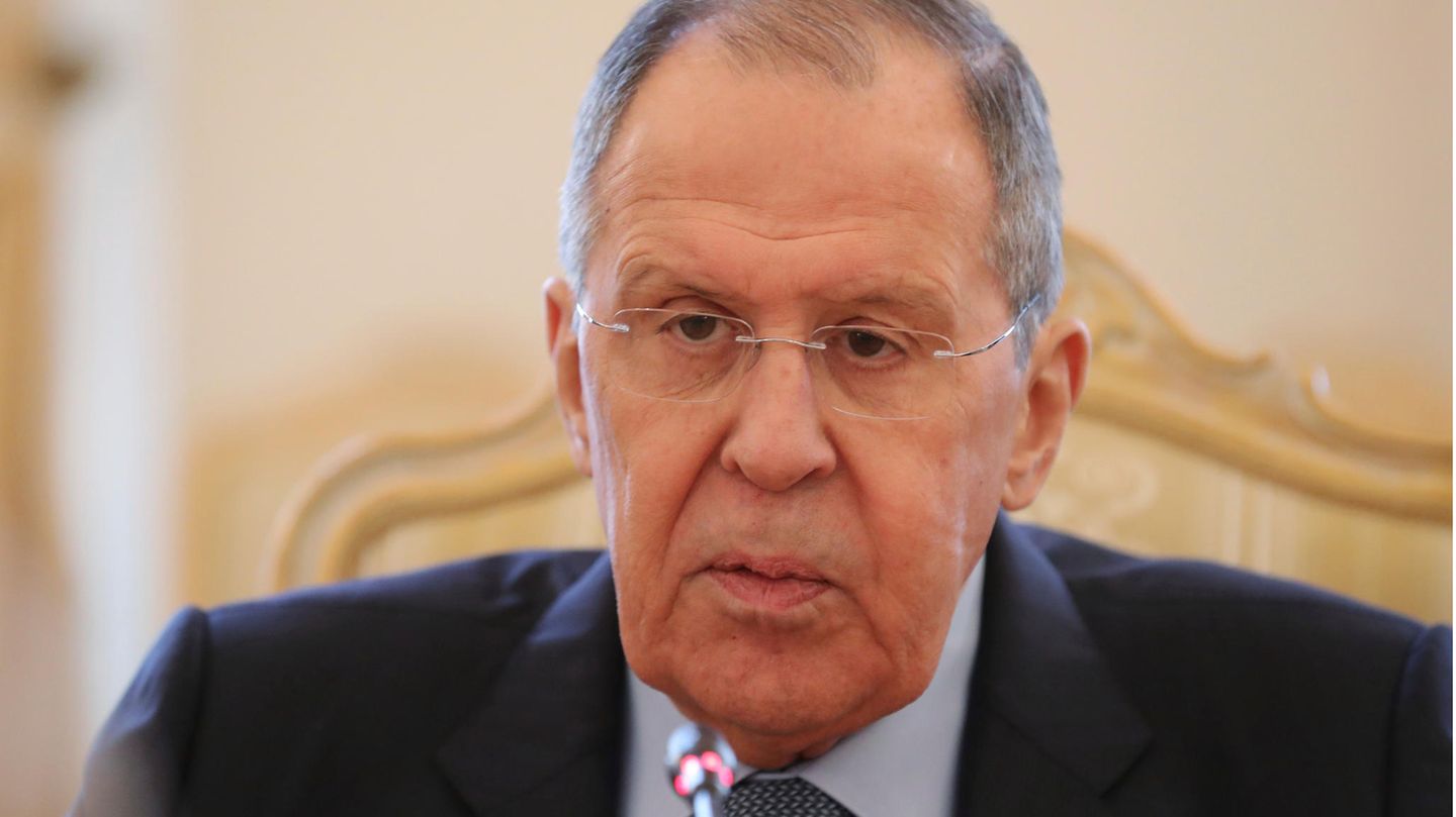 Ein alter weißer Mann mit dünnem grauem Seitenscheitel und randloser Brille sitzt im Anzug an einem Tisch