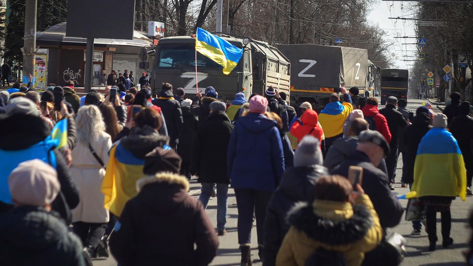 Gebiet in der Südukraine: Cherson, Ukraine. Menschen mit ukrainischen Fahnen gehen während einer Kundgebung gegen die russische Besatzung am 20. März 2022 auf Lastwagen der russischen Streitkräfte zu. Cherson, Ukraine. Menschen mit ukrainischen Fahnen gehen während einer Kundgebung gegen die russische Besatzung am 20. März 2022 auf Lastwagen der russischen Streitkräfte zu.