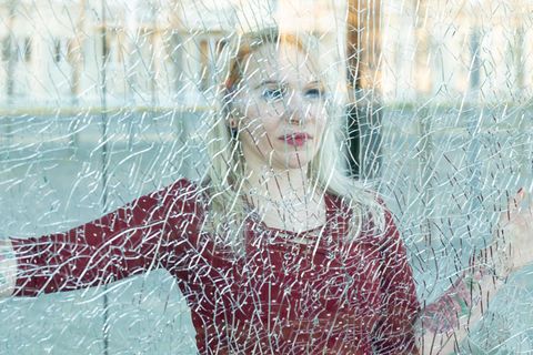 Eine blonde Frau hinter einer gesprungenen Fensterscheibe