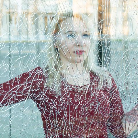 Eine blonde Frau hinter einer gesprungenen Fensterscheibe