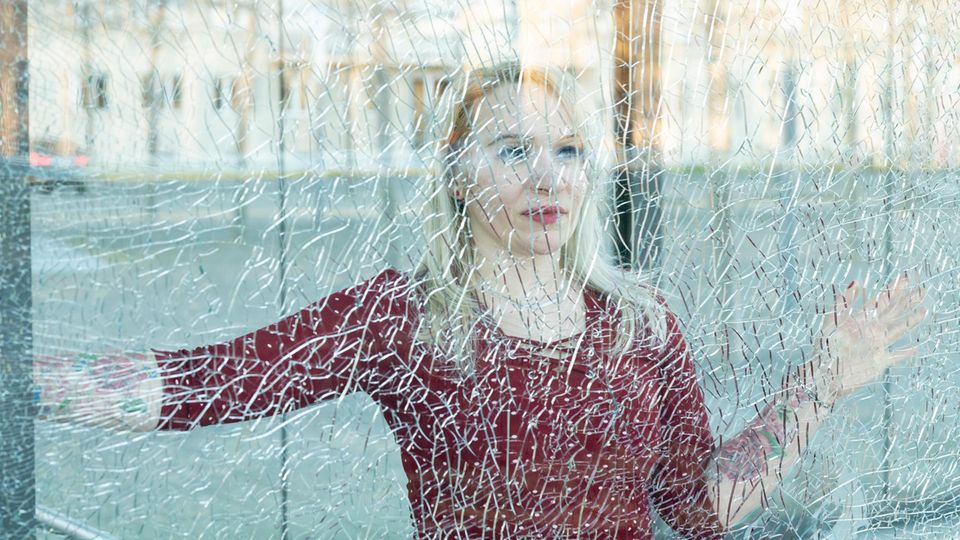 Eine blonde Frau hinter einer gesprungenen Fensterscheibe