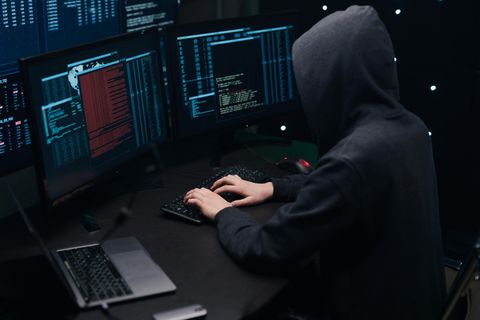 Ein Mann mit Kapuzenpullover sitzt vor mehreren Monitoren