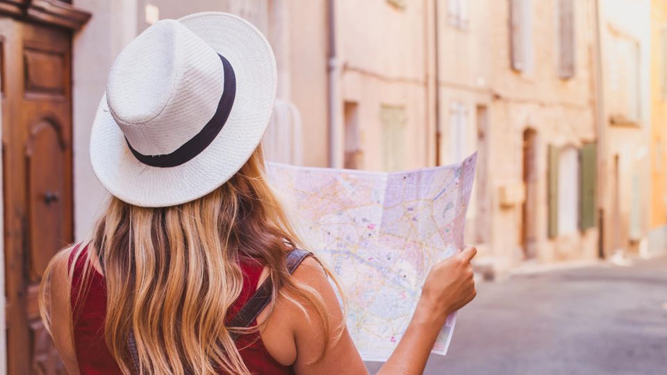 Sicher Reisen als Frau – Fünf Reiseziele für Solo-Abenteuerinnen Eine Frau mit Landkarte in einer kleinen Gasse