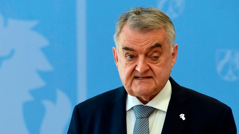 Herbert Reul Ein alter weißer Mann mit grau-weißem Seitenscheitel steht in Anzug und Krawatte vor vier Mikros von TV-Sendern und spricht