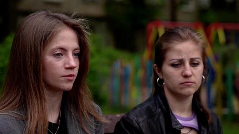 Zwei junge Frauen sitzen im Freien auf einer Bank und schauen bedrückt