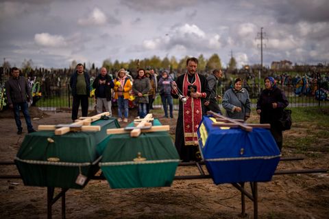 Butscha: Ein Priester segnet drei Verstorbene, die während der russischen Besatzung starben