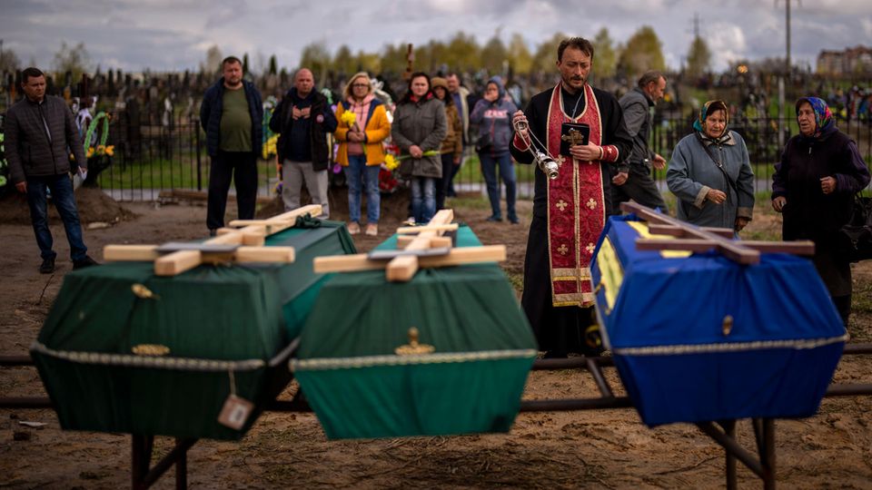 Butscha: Ein Priester segnet drei Verstorbene, die während der russischen Besatzung starben