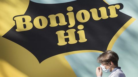 Passant vor einem Schild mit der Aufschrift "Bonjour – Hi"