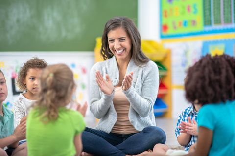 Eine lachende Lehrerin im Kreis kleiner Kinder