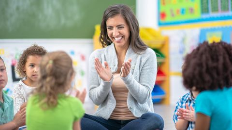 Eine lachende Lehrerin im Kreis kleiner Kinder