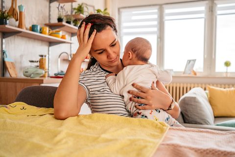 Eine Mutter hält ihr Baby auf dem arm und sieht nachdenklich dabei aus.