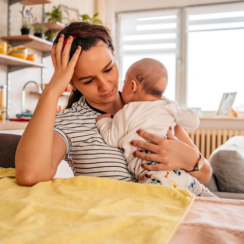 Eine Mutter hält ihr Baby auf dem arm und sieht nachdenklich dabei aus.