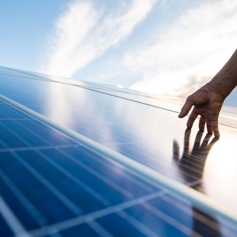 Eine Hand berührt eine Photovoltaikanlage auf einem Dach.