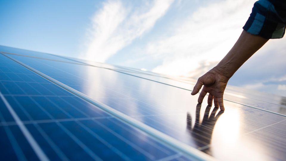 Eine Hand berührt eine Photovoltaikanlage auf einem Dach.
