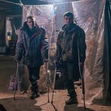 Zwei Soldaten stehen mit Krücken vor einem Behandlungszelt im Stahlwerk