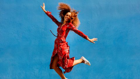 Eine Frau trägt ein rotes Wickelkleid und springt in die Luft