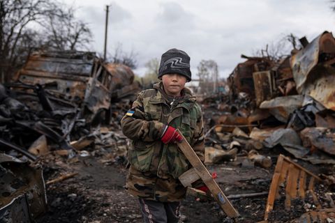 Ein Kind hält ein Spielzeuggewehr aus Holz neben zerstörten russischen Militärfahrzeugen in der Nähe von Tschernihiw