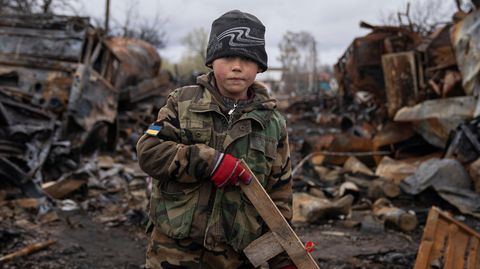 Ein Kind hält ein Spielzeuggewehr aus Holz neben zerstörten russischen Militärfahrzeugen in der Nähe von Tschernihiw