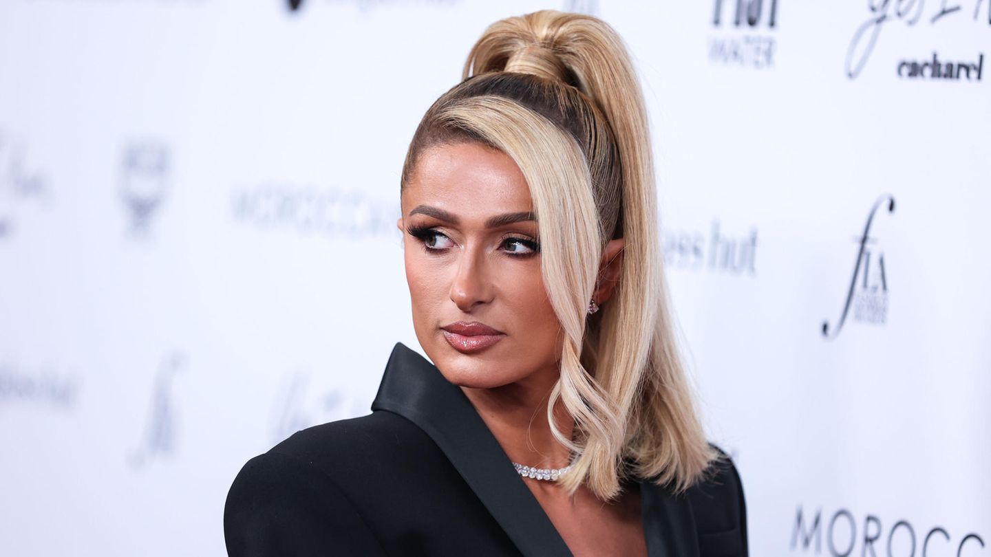 Paris Hilton steht vor einer weißen Wand mit Aufschrift. Sie unterstützt Britney Spears nach deren Fehlgeburt